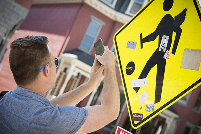man taking a photo of a yellow road sign with a black silhouette of a man walking